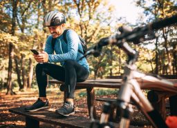 男性骑自行车的人坐在长凳上在森林里玩离线游戏在他的电话