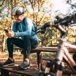 男性骑自行车的人坐在长凳上在森林里玩离线游戏在他的电话